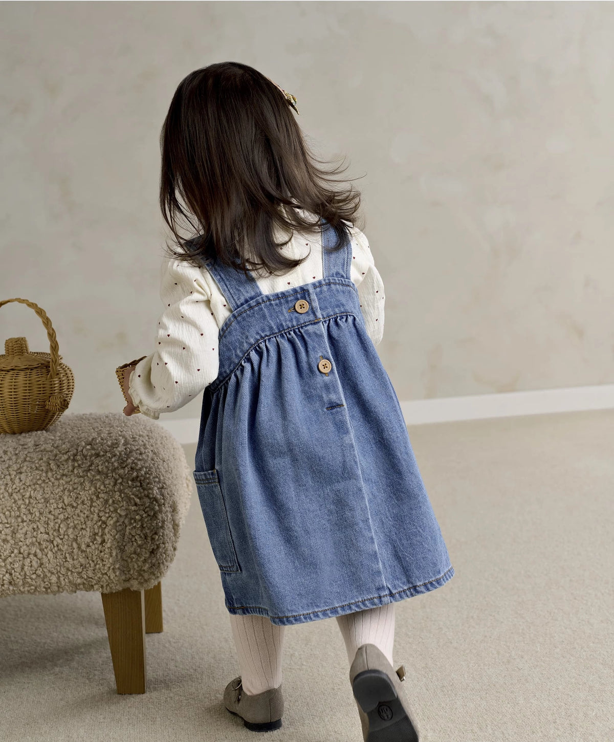 Blue denim pinafore dress over white long-sleeve bodysuit with small heart print