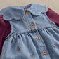 Denim dungaree bib with embroidered bows and tan buttons, burgundy ribbed sleeve cuffs
