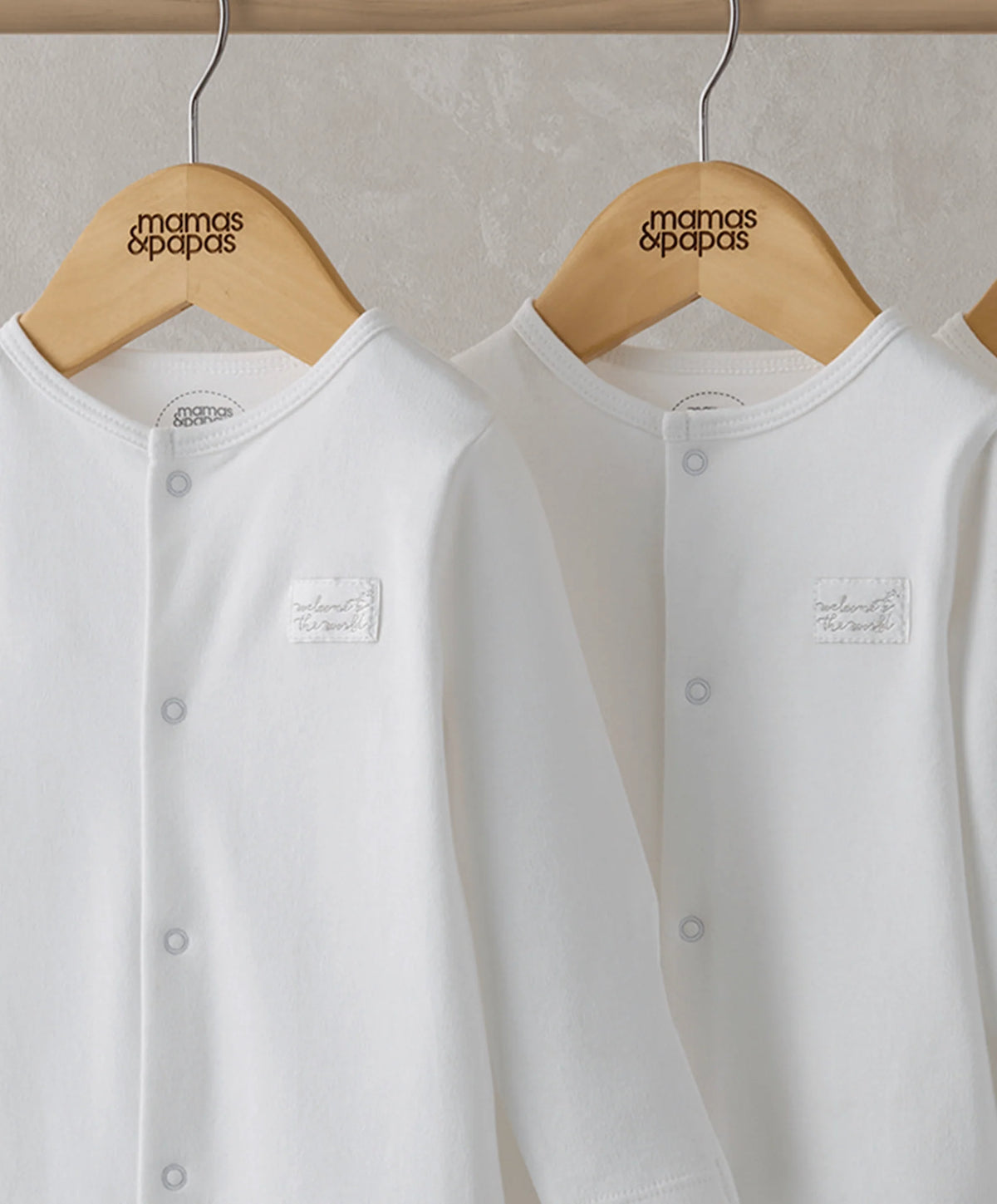 White sleepsuits close-up with snap-button front and small chest logo, pack of three