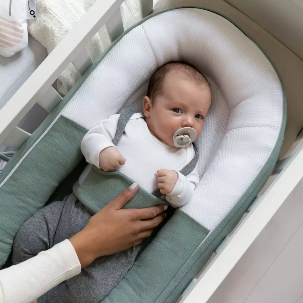 Green jersey bed reducer with white inner pad; baby wearing pacifier