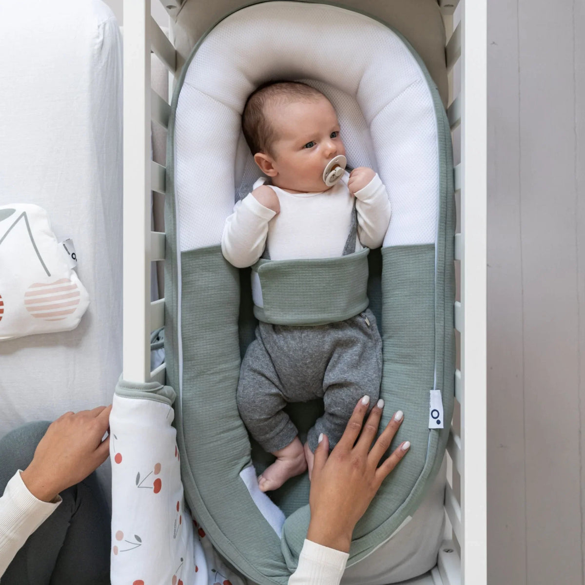 Green jersey bed reducer with white headrest pad and padded sides; baby in it