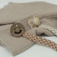 Woven pacifier clip with blush-and-ivory strap attached to two beige pacifiers