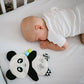 Flat cuddly panda plush toy beside a sleeping baby, white face and black ears