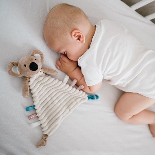 Koala cuddly flat toy near a baby's cheek, striped cream body