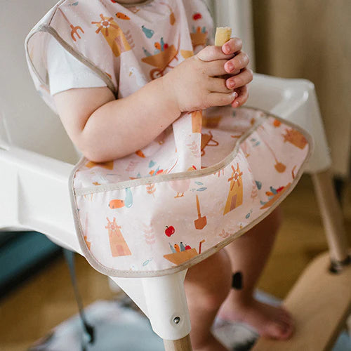 Light pink kids’ apron with farm-pattern print, worn on high chair