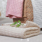 Cotton knitted blanket in beige with zigzag knit texture, folded and stacked