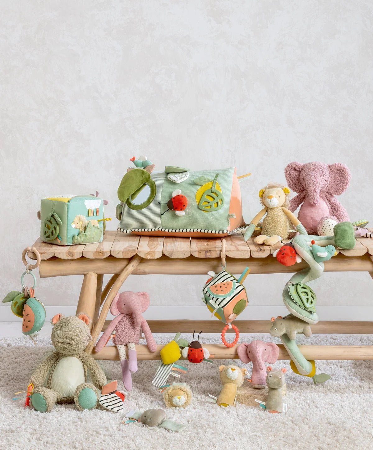 Pink elephant plush activity toy on play mat with nearby hanging toys.
