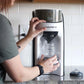 White babybrezza formula dispenser with hands holding a measuring bottle