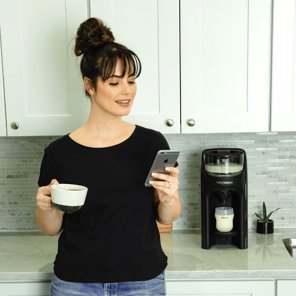 Black baby formula dispenser with a person holding a cup and smartphone nearby