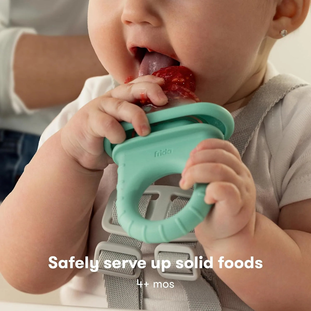 Teal baby fruit feeder held by a baby, with berry-red food in the bite cup