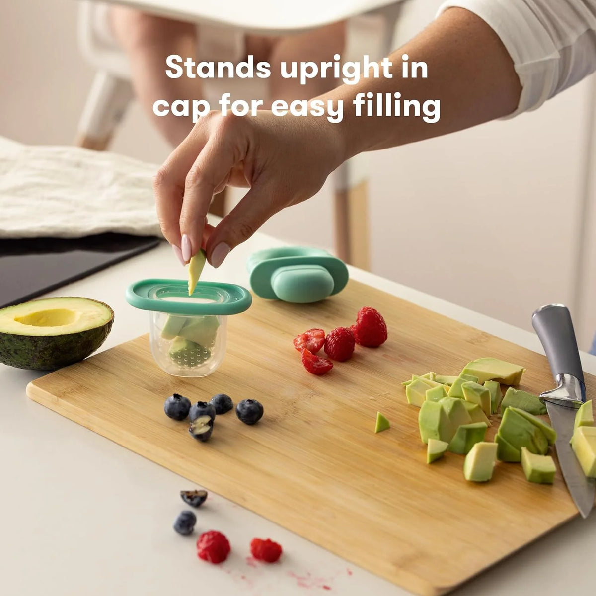 Teal push-pop baby feeder on a cutting board, with fruit and empty bite cups
