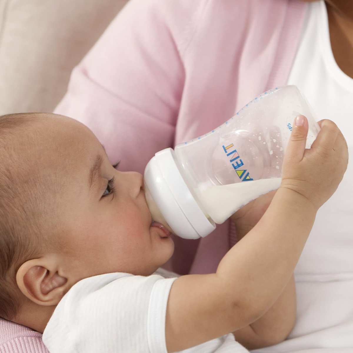 Baby drinking from a clear feeding bottle with white nipple on an adult chest