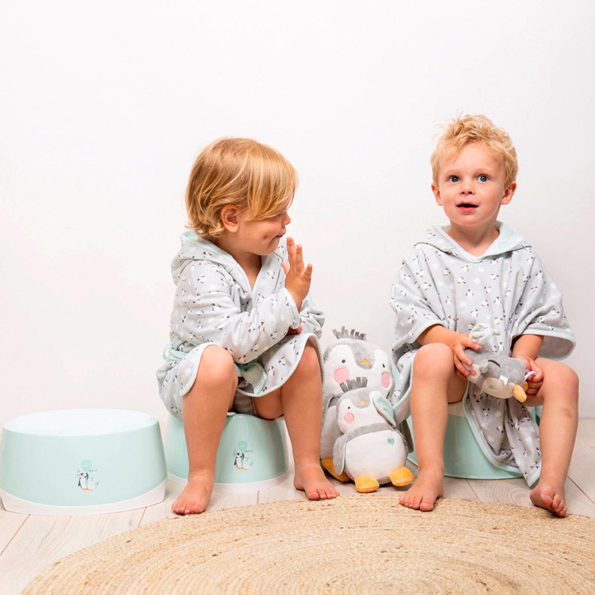 Mint potty training seat beside sitting toddler boys, plus plush toy