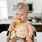 Yellow teddy-bear silicone teether with white bristle tip, held by a baby