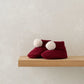 Red knit baby booties with white pom-poms and ribbed ankle cuffs