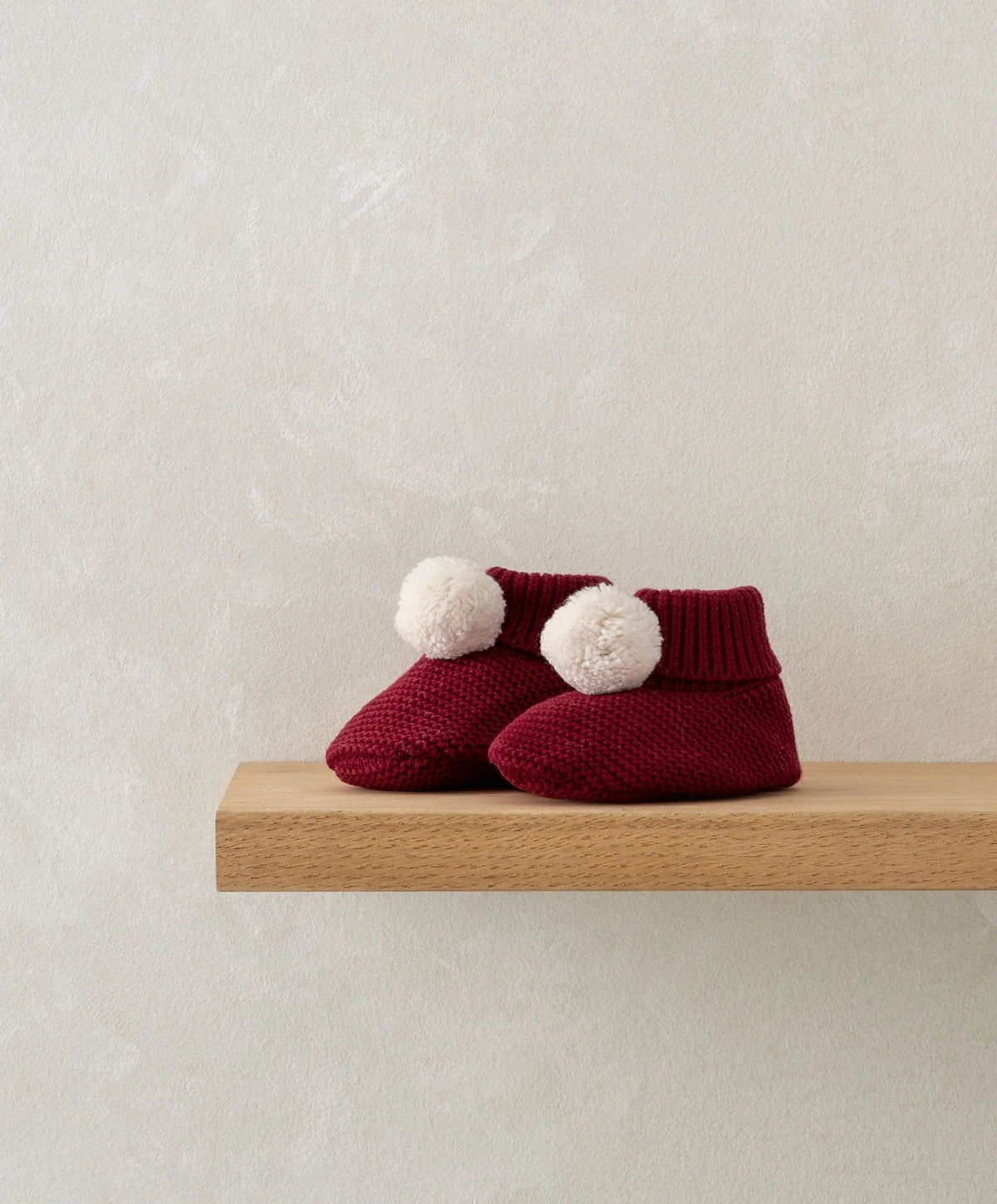 Red knit baby booties with white pom-poms and ribbed ankle cuffs