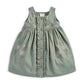 Sage green floral pinafore with gathered skirt, ruffle trim, and wooden button placket.