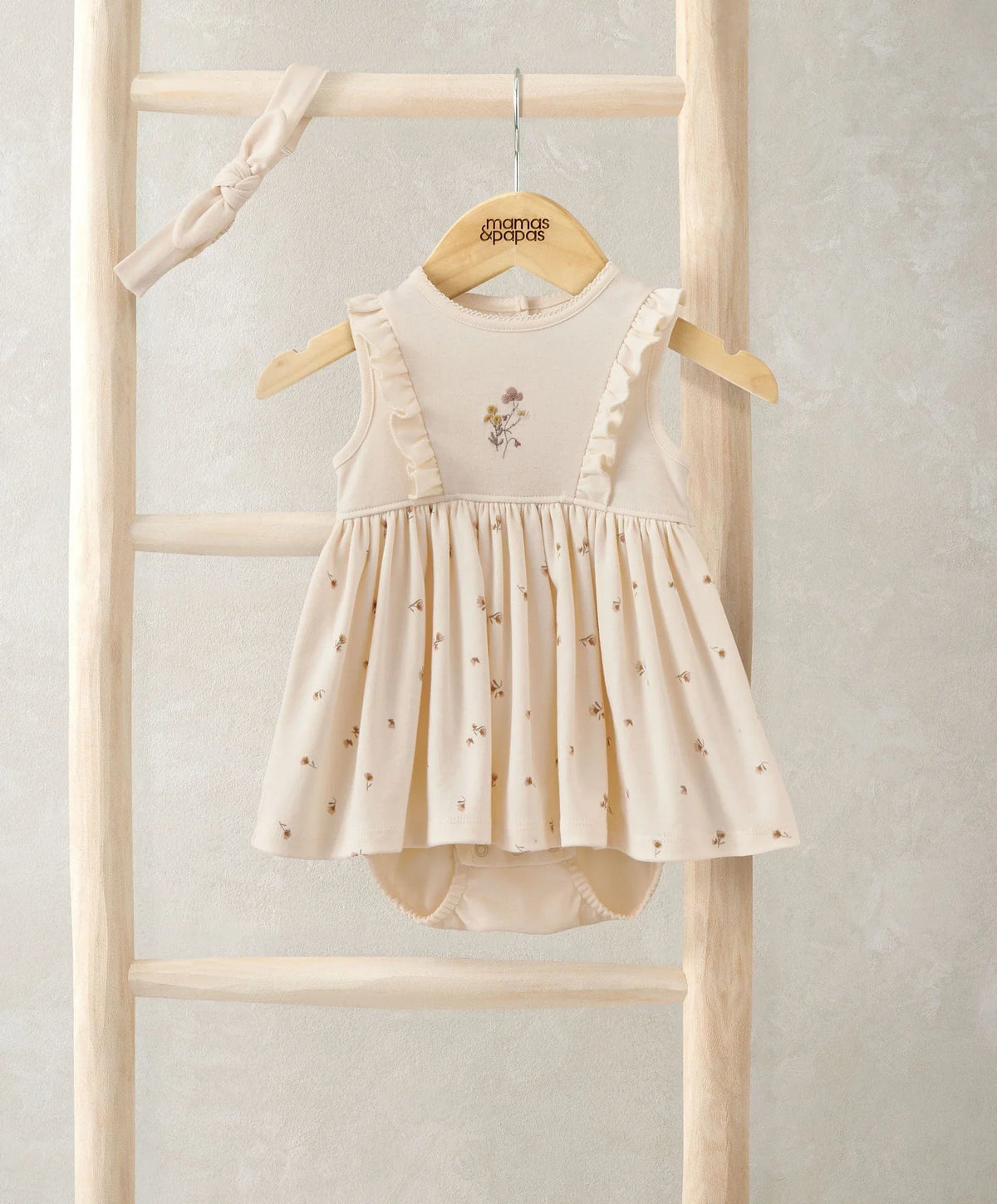 Cream mock skirt romper with ruffled shoulder straps, floral applique, and matching headband