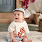 Baby in cream lobster graphic t-shirt with light blue shorts, sitting pose