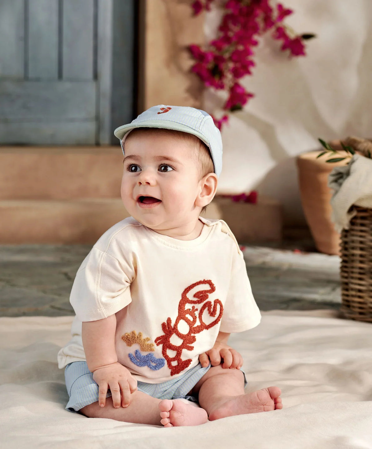 Baby in cream lobster graphic t-shirt with light blue shorts, sitting pose