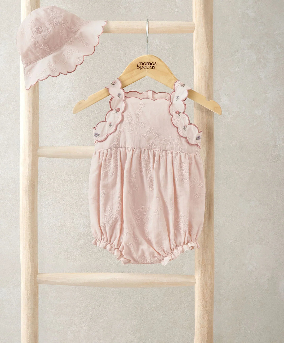 Light pink baby romper with scalloped lace trim and gathered waist; matching sun hat