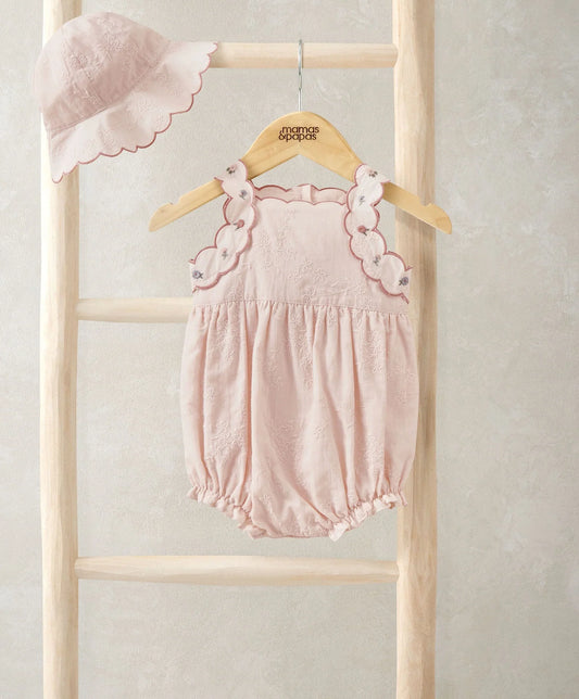 Light pink baby romper with scalloped lace trim and gathered waist; matching sun hat