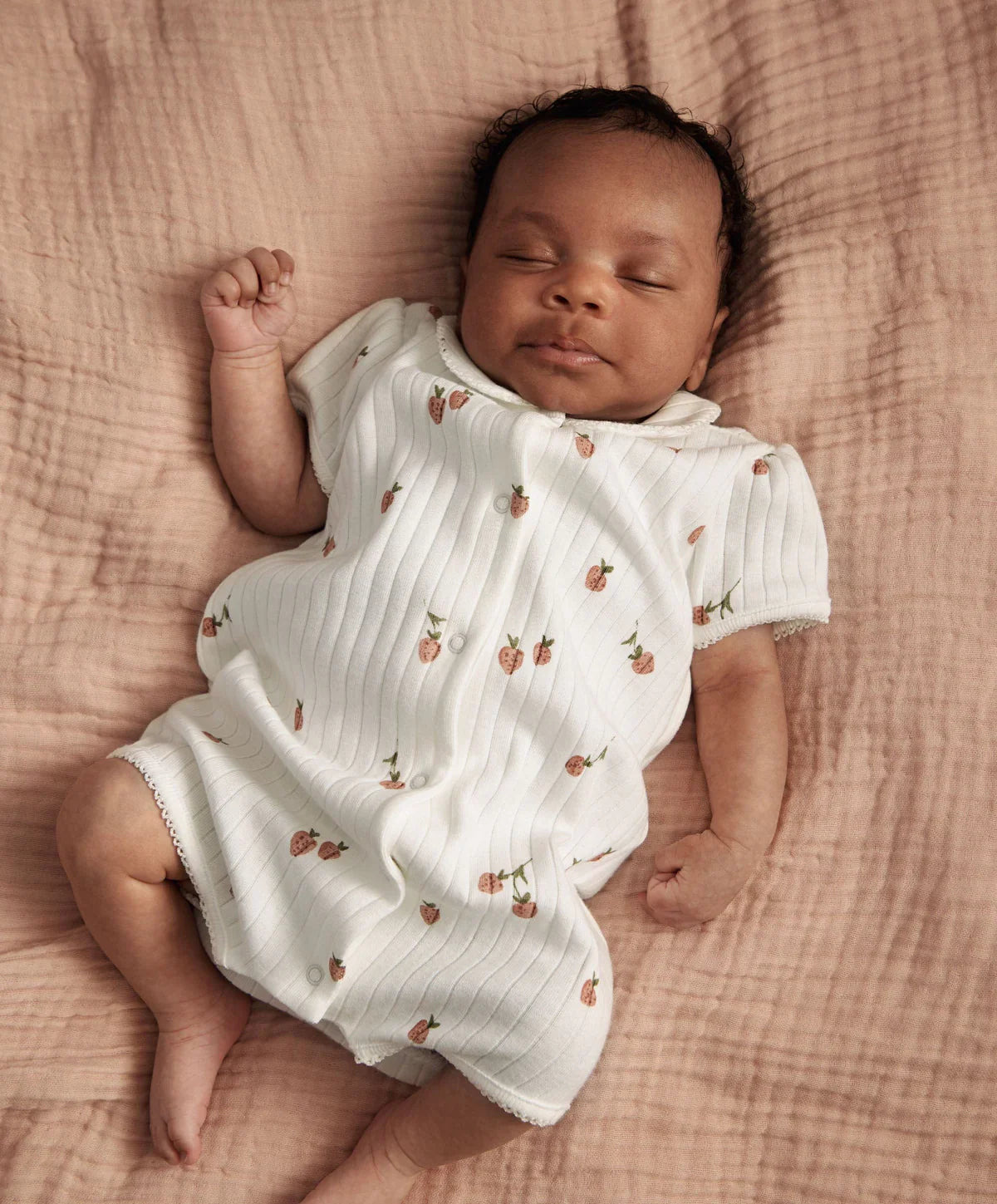 Strawberry-print short-sleeve romper worn by a sleeping baby, button front