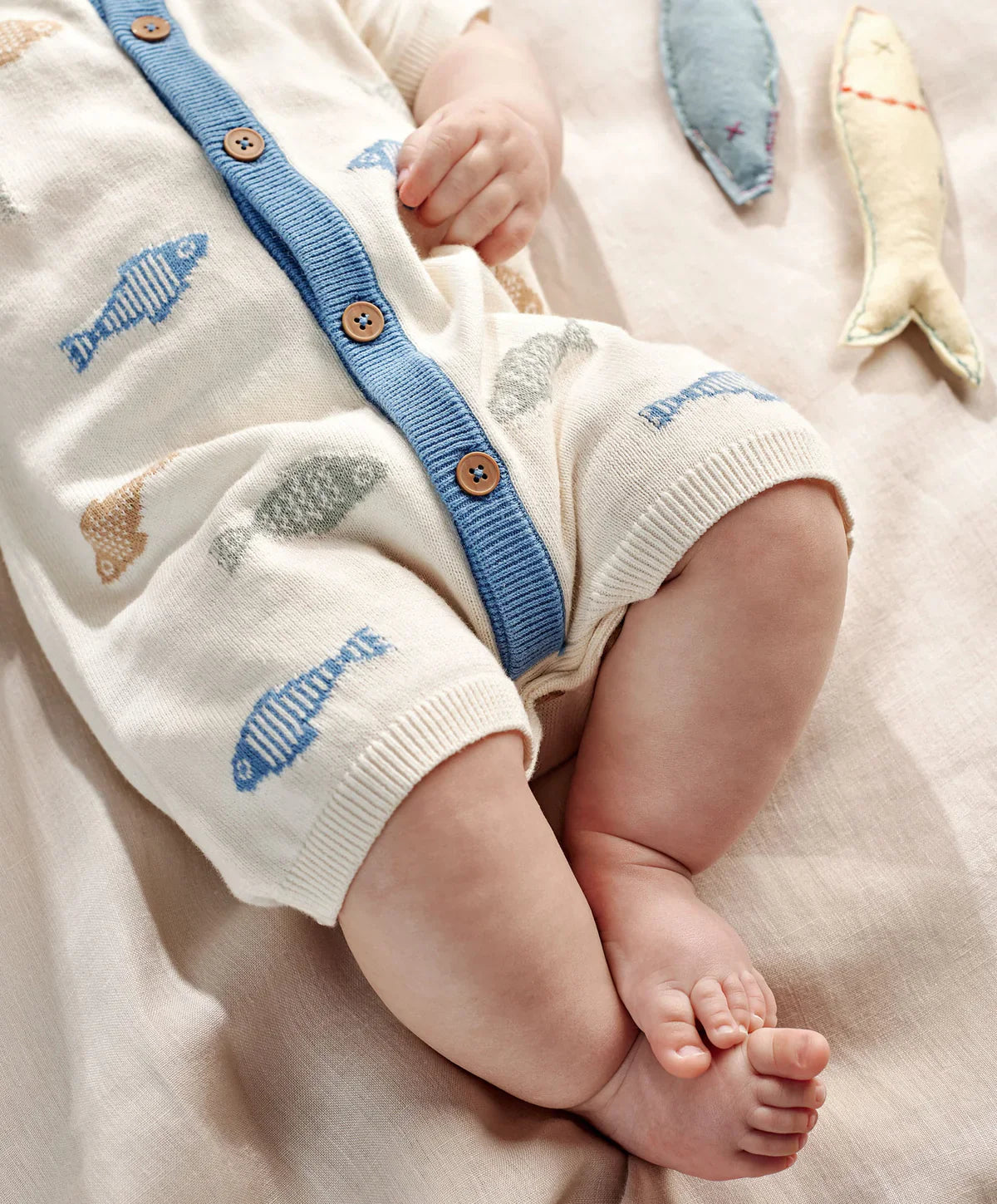 Cream romper close-up: blue button placket, fish knit pattern, ribbed cuffs, leg openings