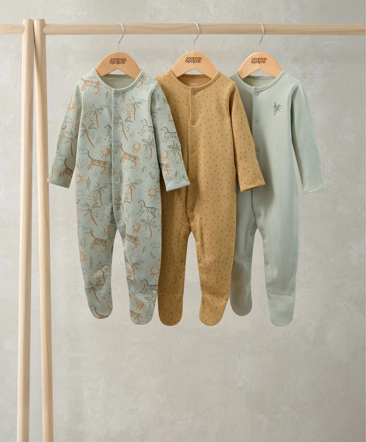 Three hanging baby sleepsuits in mint green, tan dots, and light blue safari print.