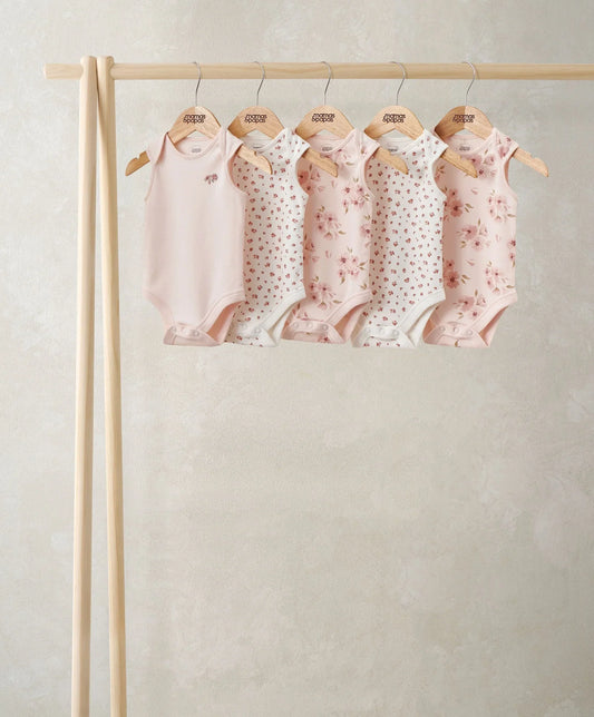 Set of five short-sleeve bodysuits hanging on wooden rail, floral and dot patterns in pink tones