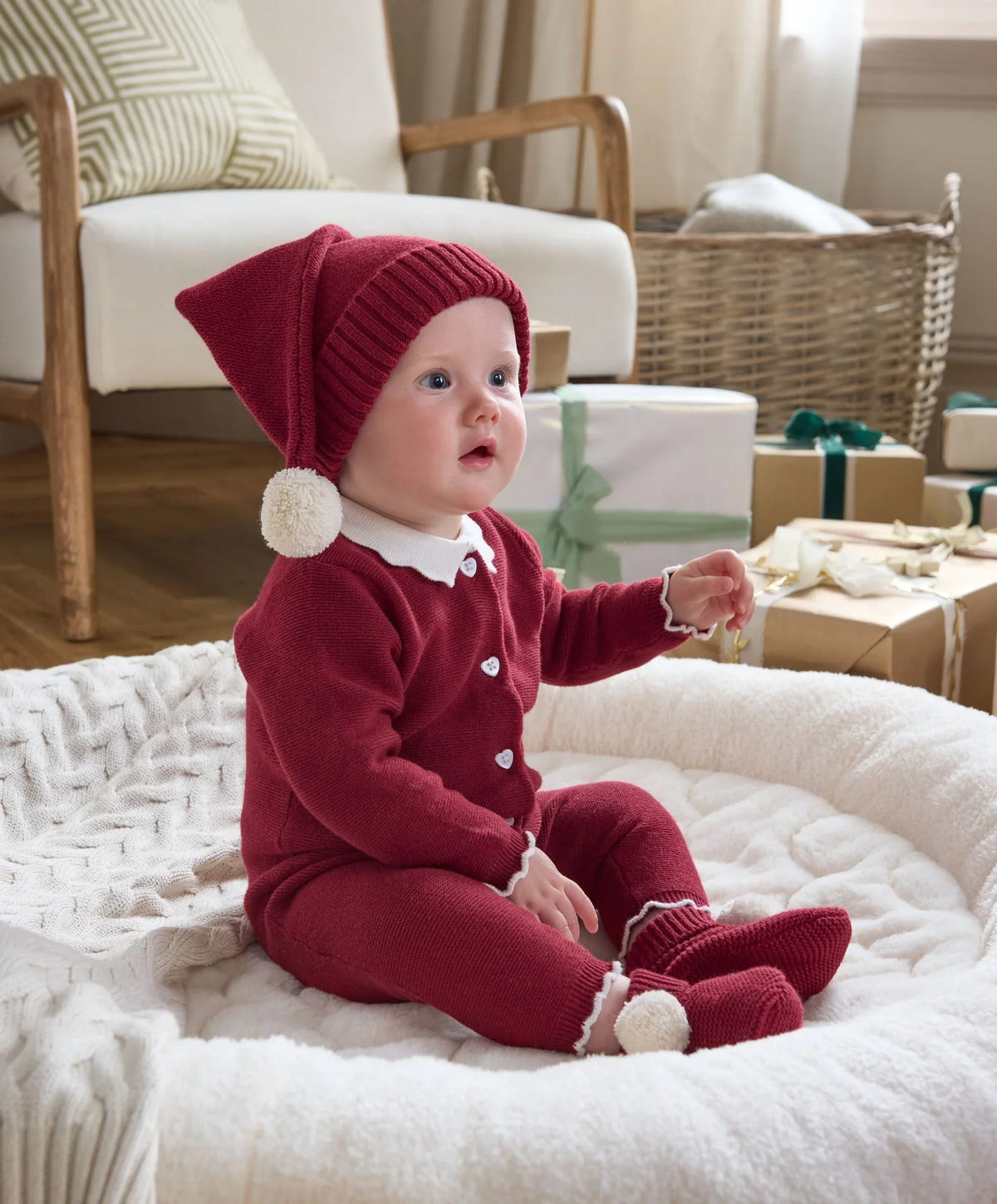 Red knitted baby hat on baby with ribbed cuff and white pom-pom