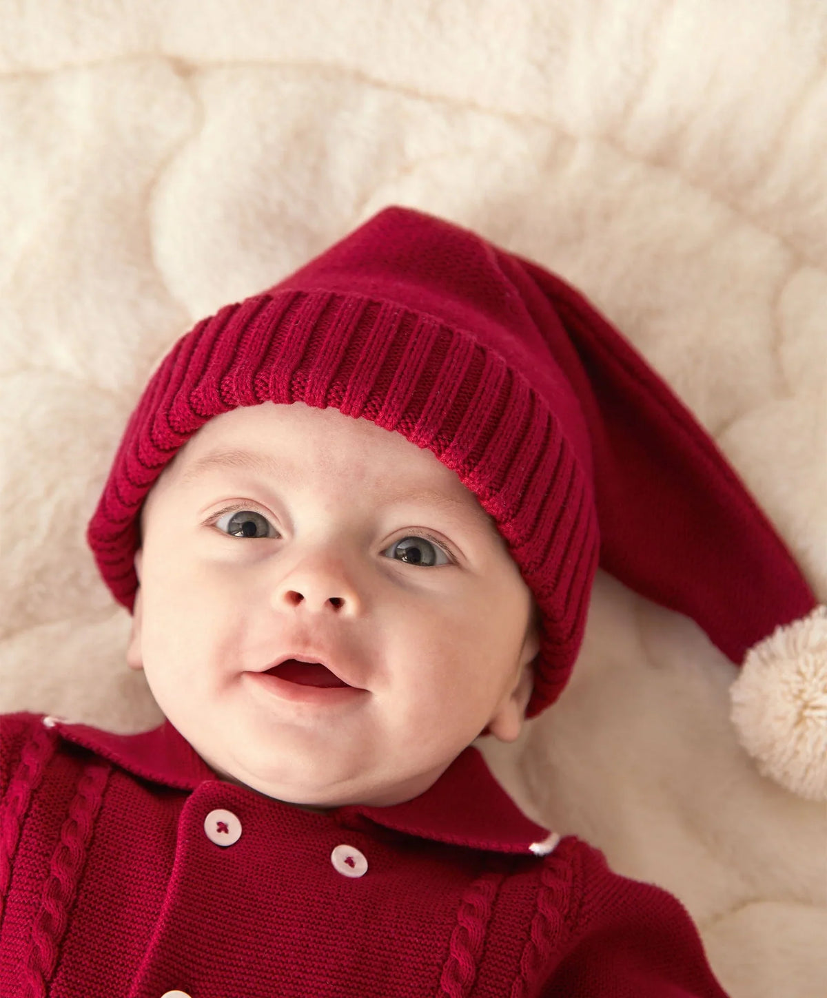 Red knit baby hat close-up with ribbed edge and white pom-pom
