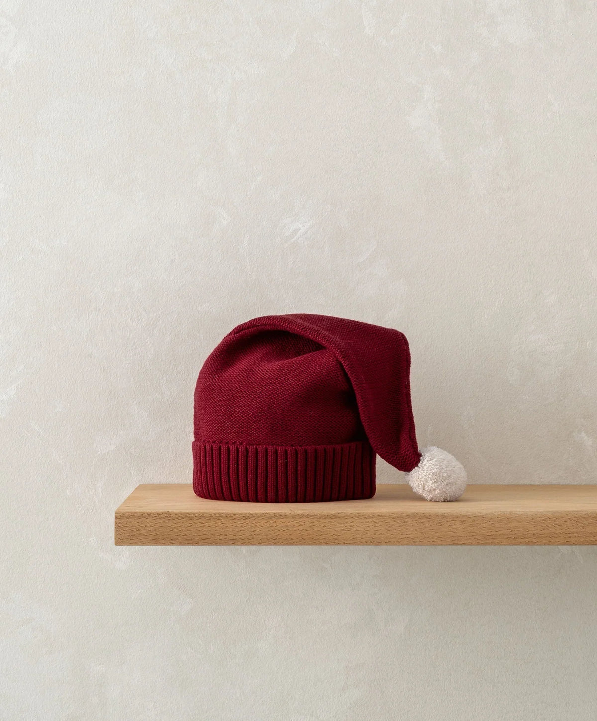 Red knitted baby hat with ribbed cuff and white pom-pom