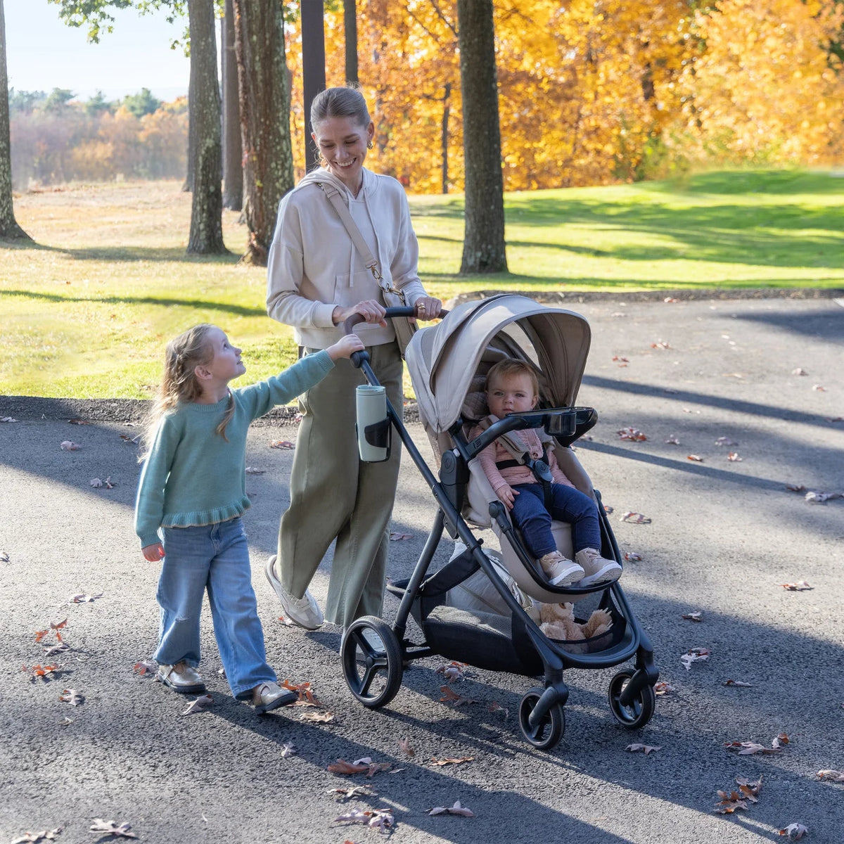 Baby stroller on black frame with light beige canopy in park.