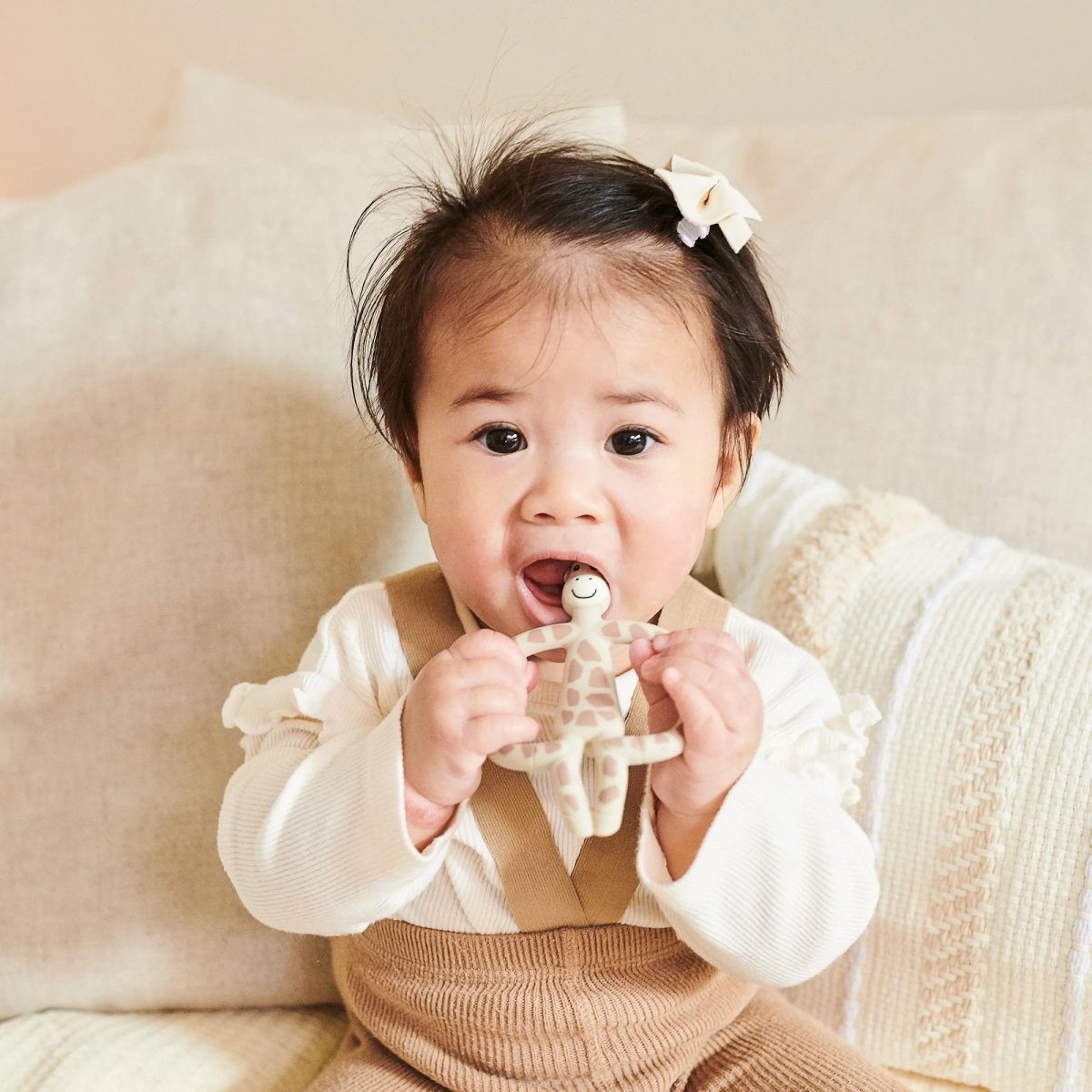 Giraffe animal teether with muslin cloth, held by baby; beige and brown