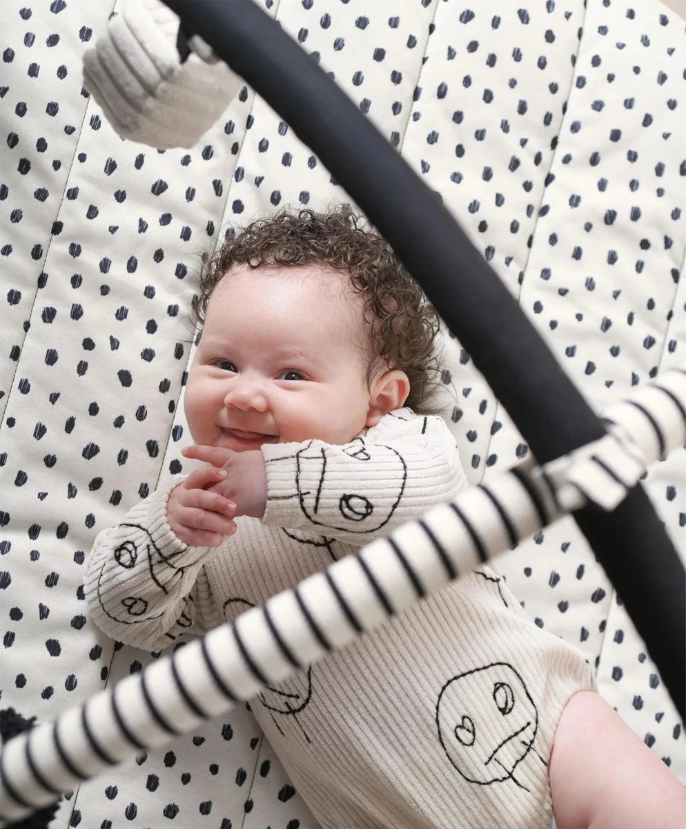 Round play mat with black-and-white dot pattern and hanging toy arch