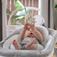 Baby resting in gray cushioned swing seat with plush toy overhead