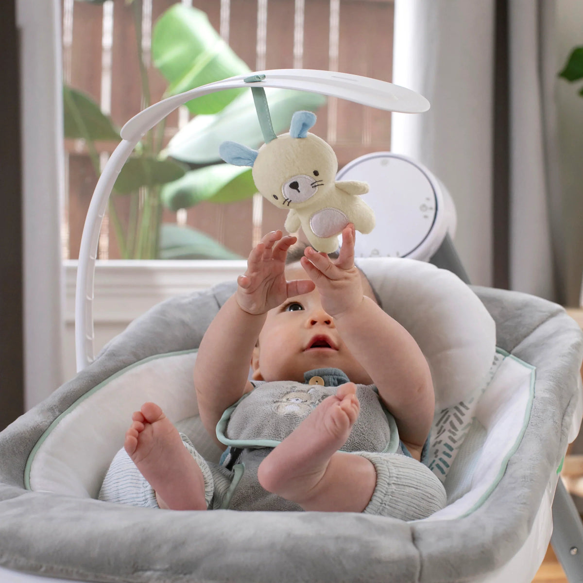Baby resting in gray cushioned swing seat with plush toy overhead