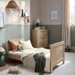 Light oak cotbed with slat rails and short end panels, with blankets on mattress