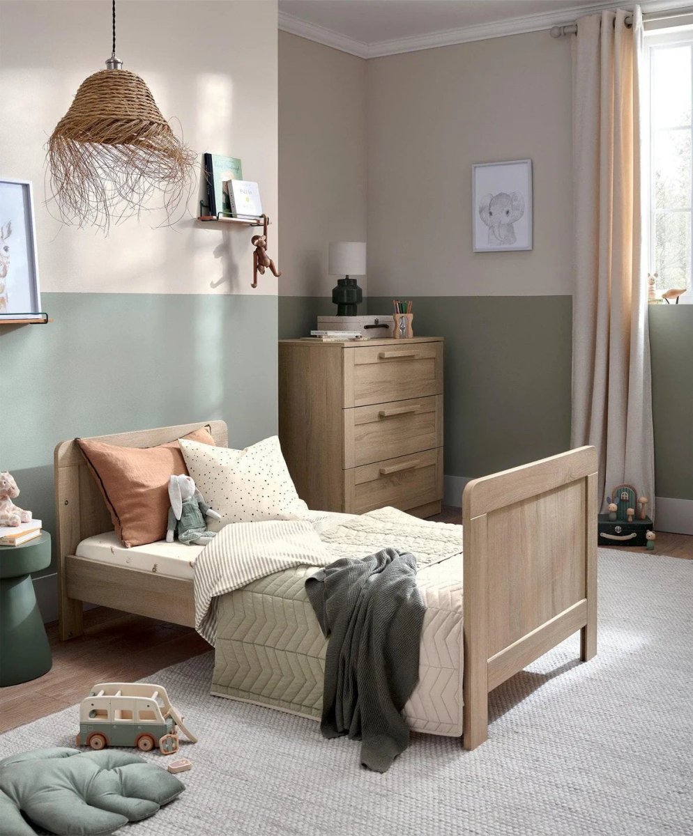 Light oak cotbed with slat rails and short end panels, with blankets on mattress