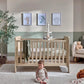 Light oak cotbed with slat rails and hanging mobile, toddler kneeling on rug