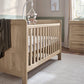 Light oak cotbed with paneled ends and vertical slat sides, plus hanging mobile
