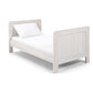 Light gray cotbed with vertical slat rails, cushioned end panel details, studio view