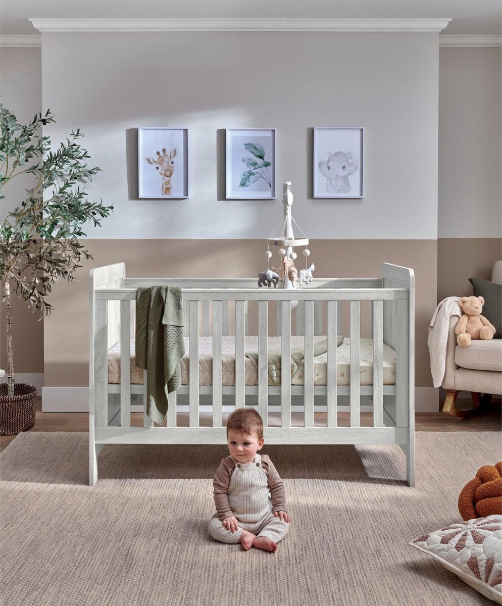 Light gray cotbed with vertical slat rails and raised end panels, nursery setup