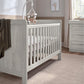 Light gray wood cotbed with vertical rails and two end panels, side view