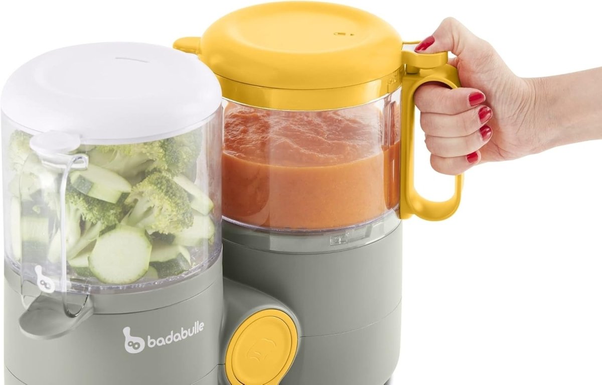 Baby food processor with clear blending jars, gray base, and yellow lid being held