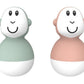 Two bath wobbler toys with smiling faces in mint and peach, rounded with small side nubs.