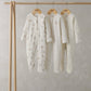 Three light cream baby sleepsuits on wooden hangers, long sleeves with bear prints