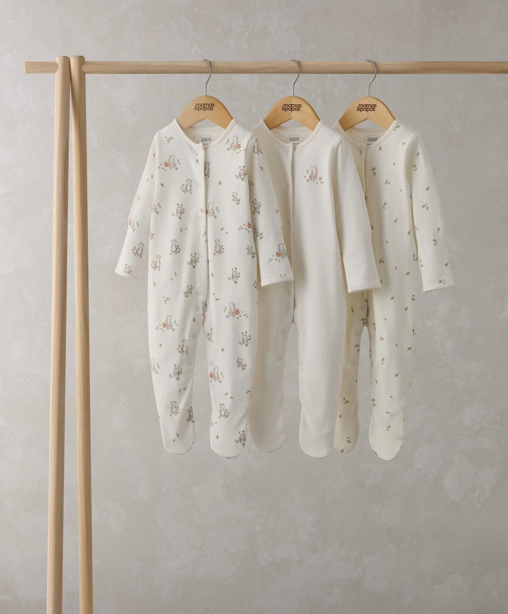 Three light cream baby sleepsuits on wooden hangers, long sleeves with bear prints