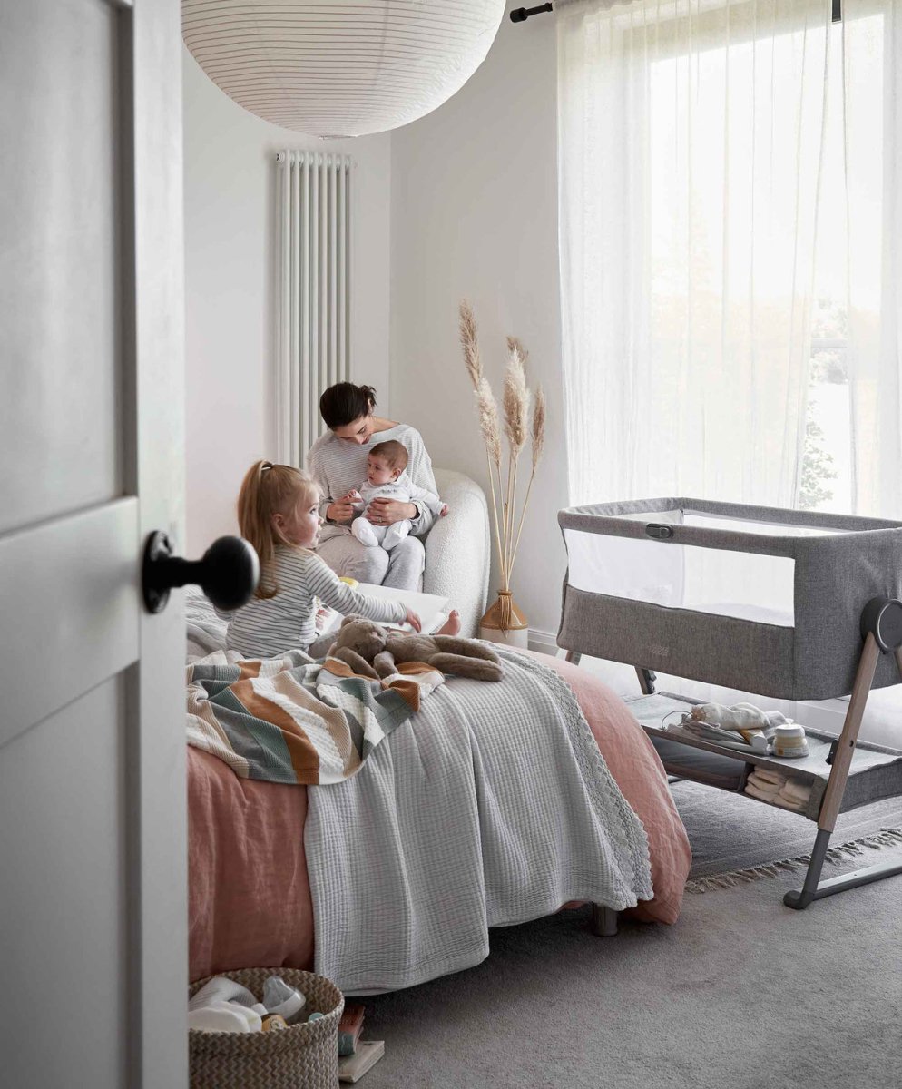 Grey bedside crib beside a bed with soft mattress and raised side rail